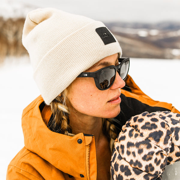 Woman in the snow wearing a beanie, black sunglasses and gloves