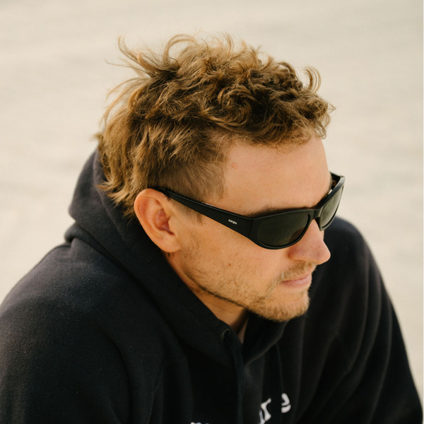 Man wearing sunglasses and a dark hoodie against a neutral background