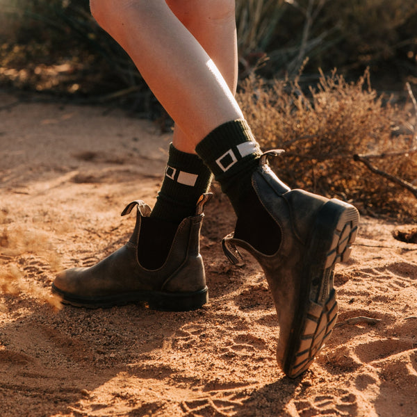Someone wearing boots and socks walking on red dirt