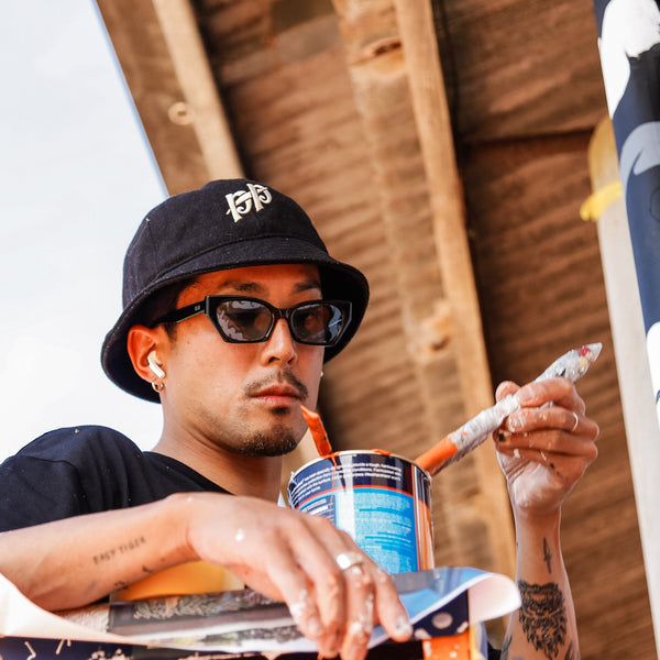 Artist Kentaro Yoshida wearing clear frame sunglasses with blue lenses whilst painting a mural