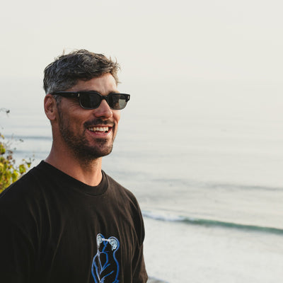 Jay Davies wearing surf sunglasses looking out at the ocean smiling