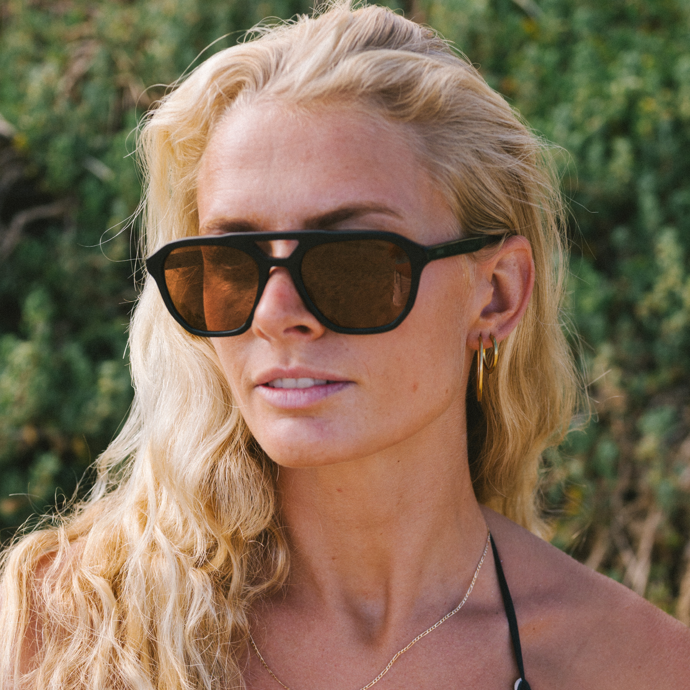 Woman wearing aviator sunglasses with leaves in the background