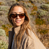 Blonde girl wearing sunglasses with a brown lens and smiling