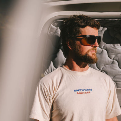 Man wearing dark square sunglasses looking to the side out into the distance in a white t shirt
