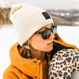 Woman in snow wearing a beanie and a leopard print glove and black sunglasses