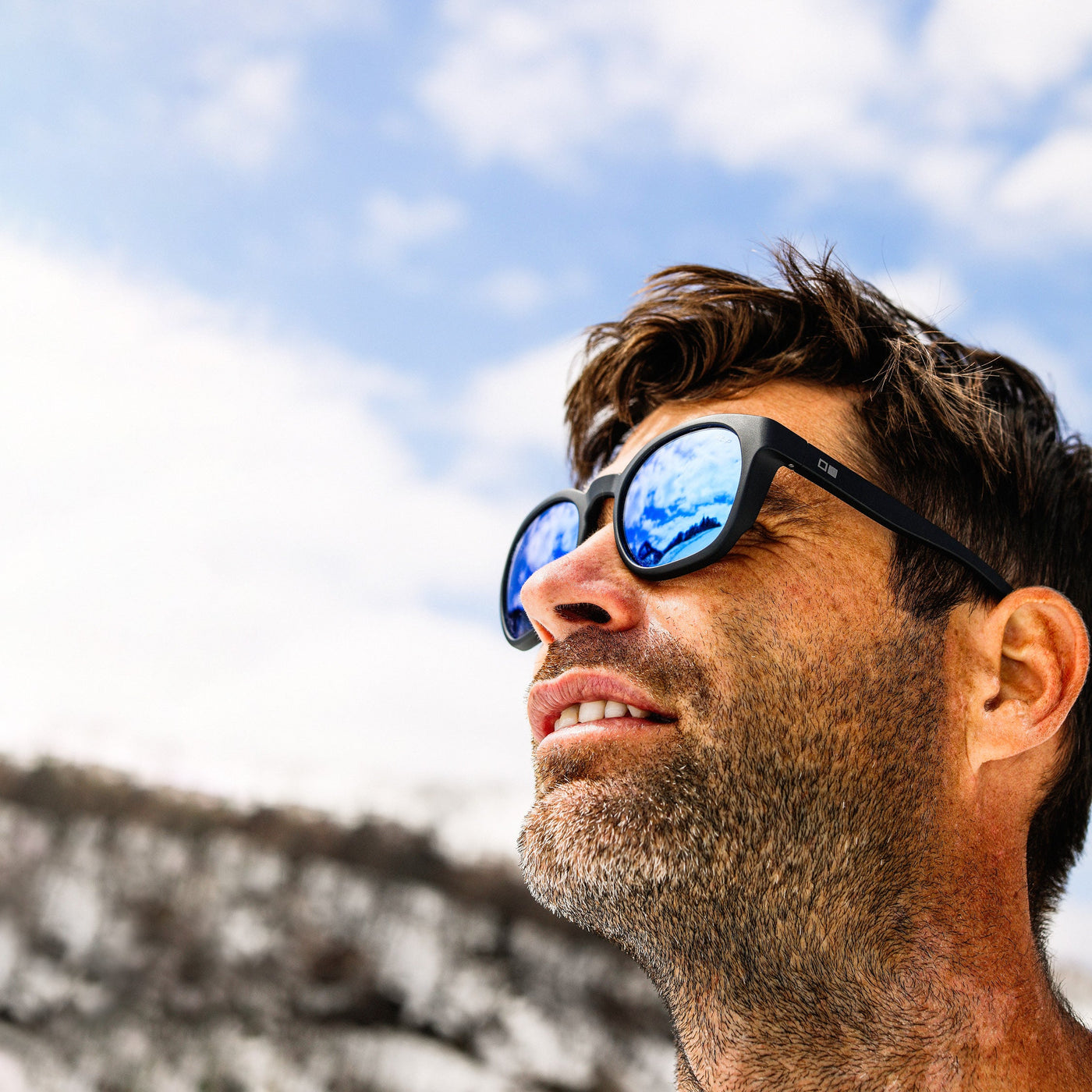 Man in snowy mountains wearing blue reflect lens sunglasses and smiling looking upward