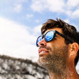 Man in snowy mountains wearing blue reflect lens sunglasses and smiling looking upward