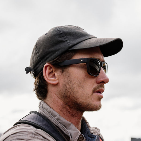 man wearing hat and black sunglasses from side on. 