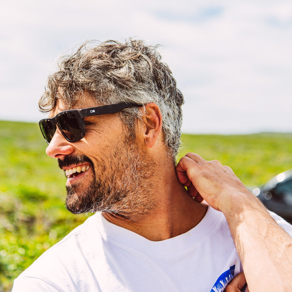 Jay Davies wearing Black sunglasses with the OTIS eyewear logo on the temple scratching his neck and smiling