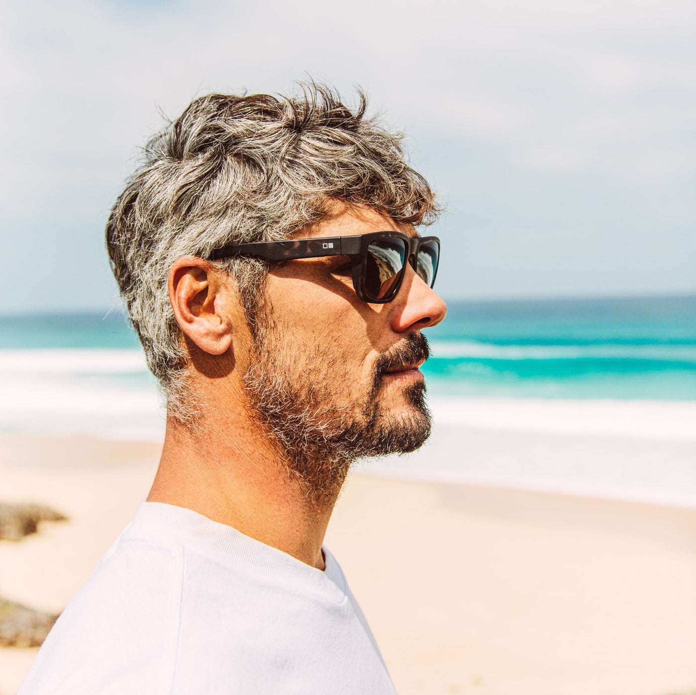 Jay Davies wearing black tort sunglasses looking at the ocean