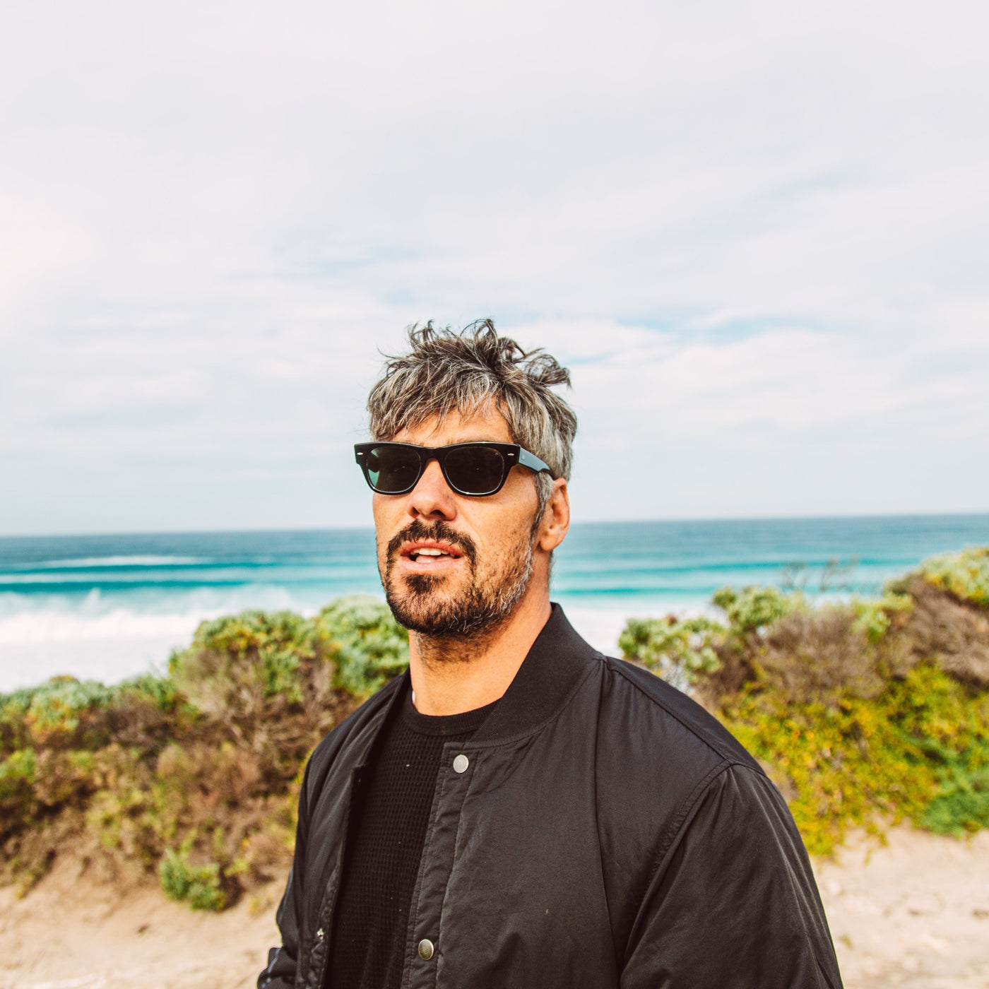 Jay Davies wearing black wayfarer sunglasses in front of the ocean