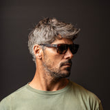 A headshot of Jay Davies wearing a green top top and brown tort sunglasses