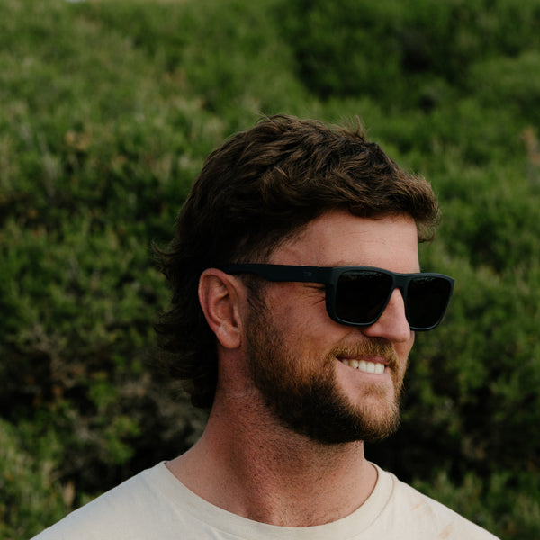 Man wearing Black Sunglasses smiling in front of a bush