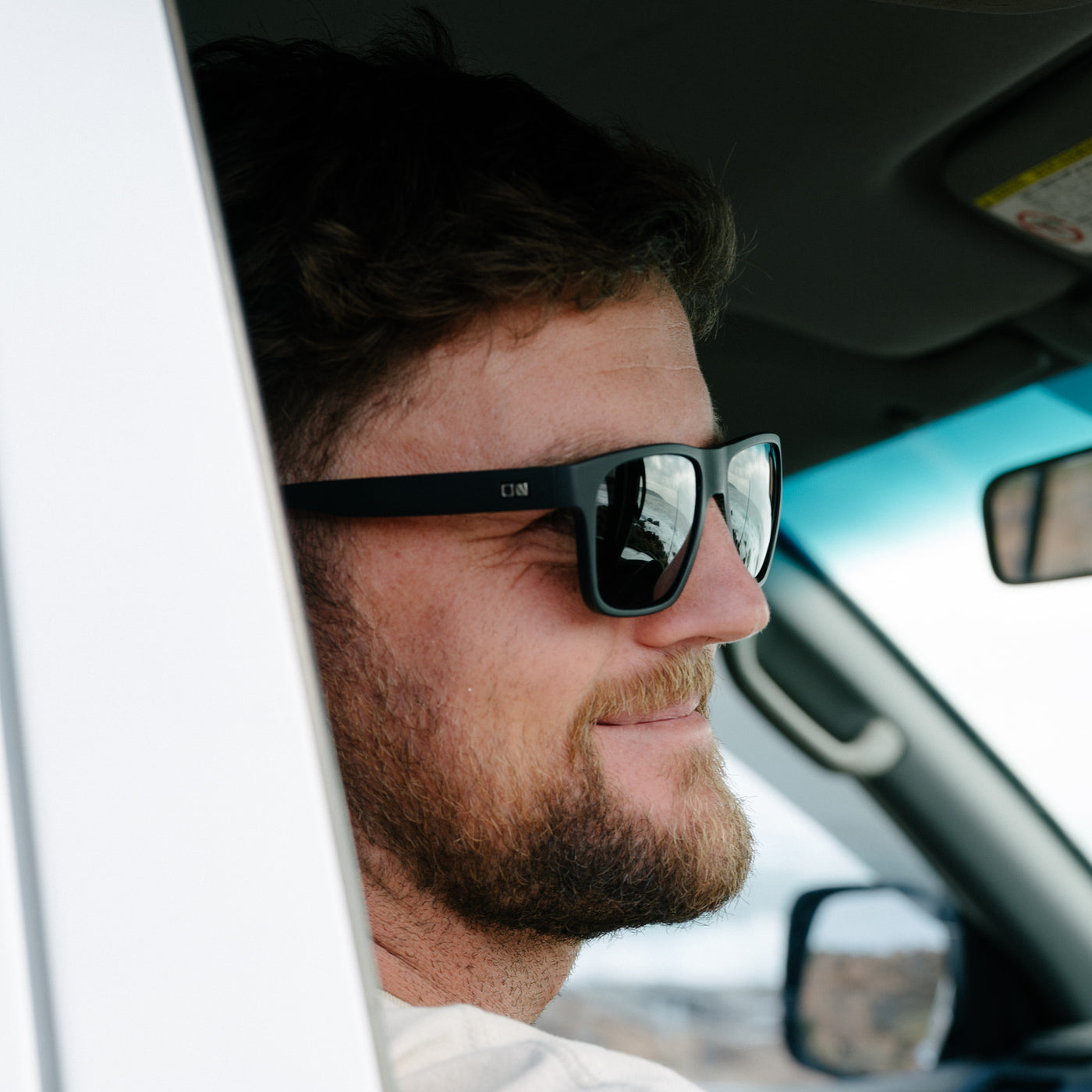 Man looking outside car window wearing sunglasses and smiling