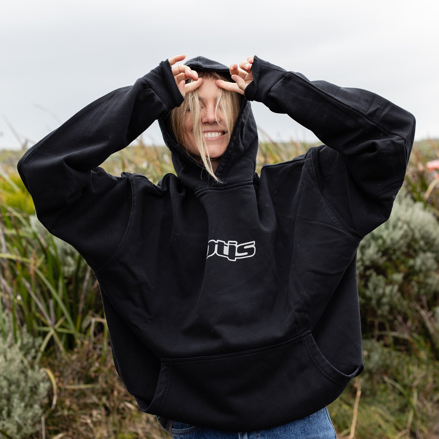 Person wearing a black hoodie with a logo in an outdoor setting