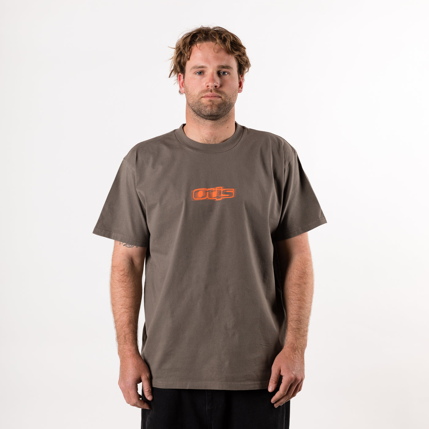 Man wearing a brown t-shirt with an orange OTIS logo on a white background