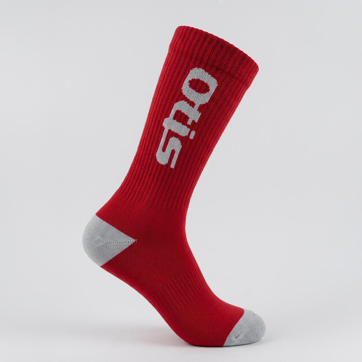 A single red crew sock with a gray heel and toe, featuring the brand name 'otis' in white knit on the side, photographed against a light gray studio background.