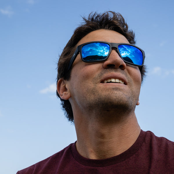 Man smiling and looking up at the blue sky wearing blue reflect sunglasses.