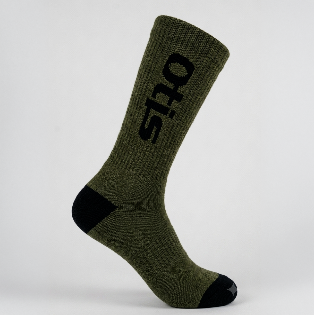 An olive green crew sock with black accents on the heel, toe, and a large black 'otis' logo printed vertically on the side, shown against a light gray studio background.