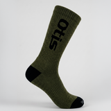 An olive green crew sock with black accents on the heel, toe, and a large black 'otis' logo printed vertically on the side, shown against a light gray studio background.