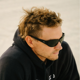 Man wearing sunglasses and a dark hoodie against a neutral background