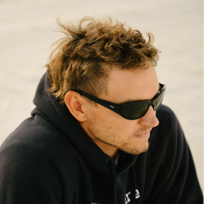 Man wearing sunglasses and a dark hoodie against a neutral background