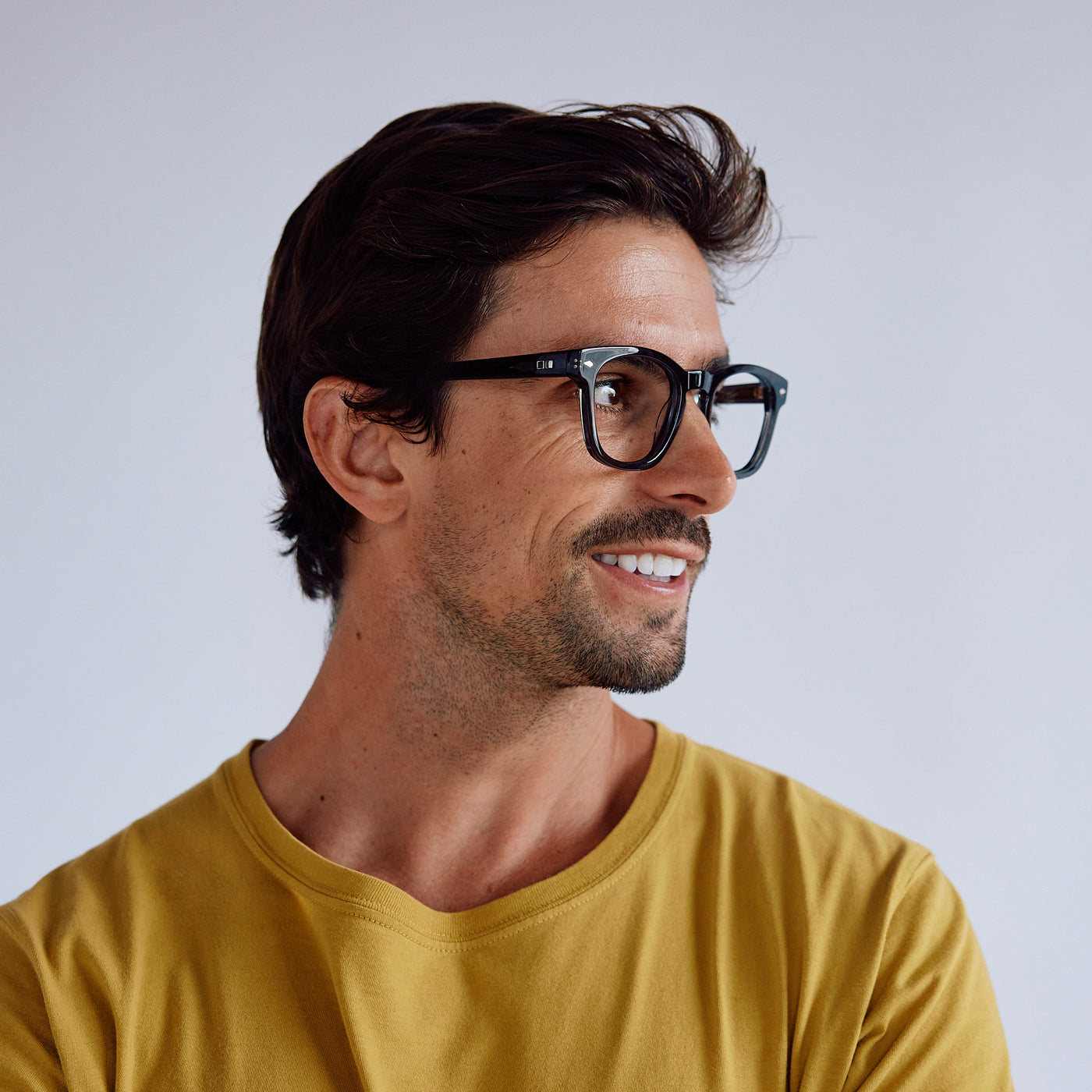 Man wearing yellow t shirt and glasses in front of white wall looking to the side