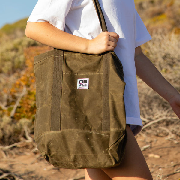 Person holding Army Green Waxed canvas tote bag with OTIS logo stitched onto front