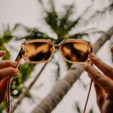 Hands holding up golden translucent sunglasses to the sky 