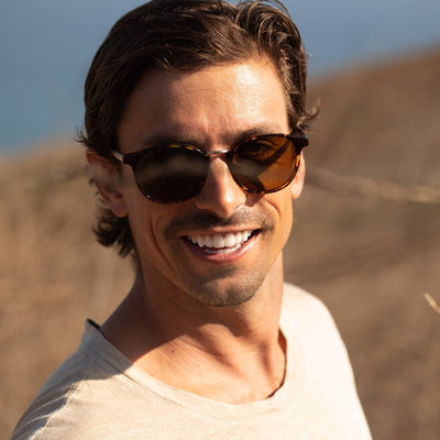 Man smiling and wearing round tort mineral glass sunglasses