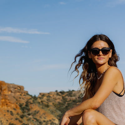 Woman smiling and wearing OTIS Eyewear round cat eye sunglasses in nature