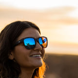 Woman smiling and wearing OTIS Eyewear round cat eye sunglasses with blue reflective lenses