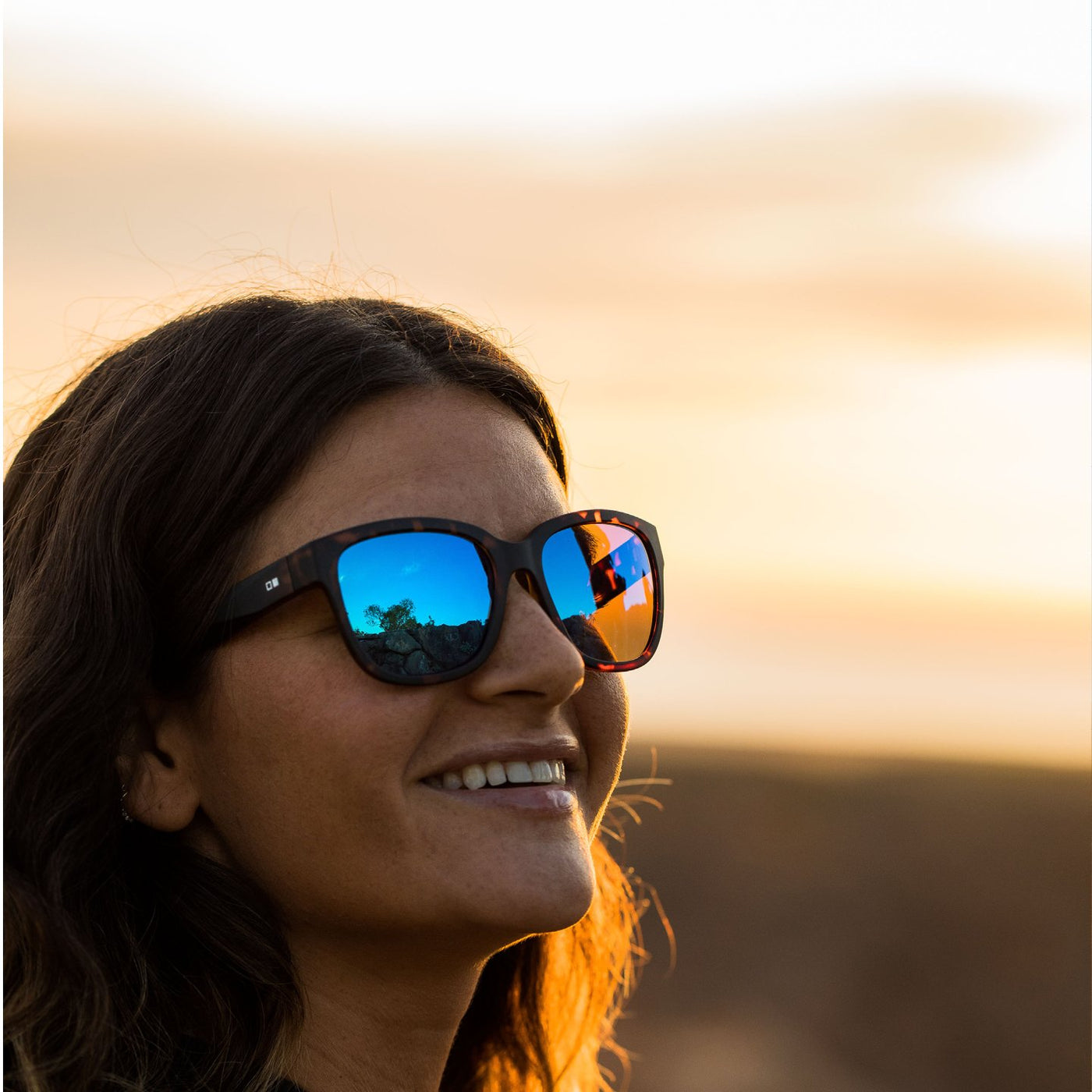 Woman smiling and wearing OTIS Eyewear round cat eye sunglasses with blue reflective lenses