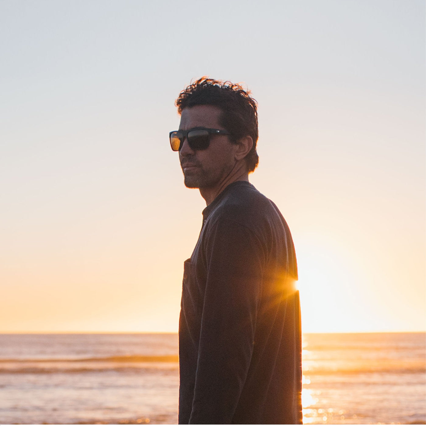 Greg Long standing in front of the ocean at sunset wearing black sunglasses