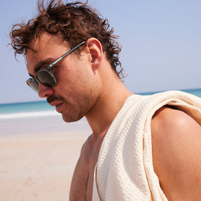 Man with towel over his shoulder looking down wearing blue crystal sunglasses