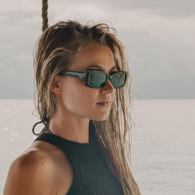 Imogen Caldwell wearing black rectangle sunglasses looking out to the ocean