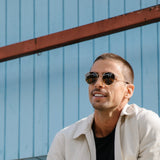 Man wearing round wire frame sunglasses in front of a blue wall