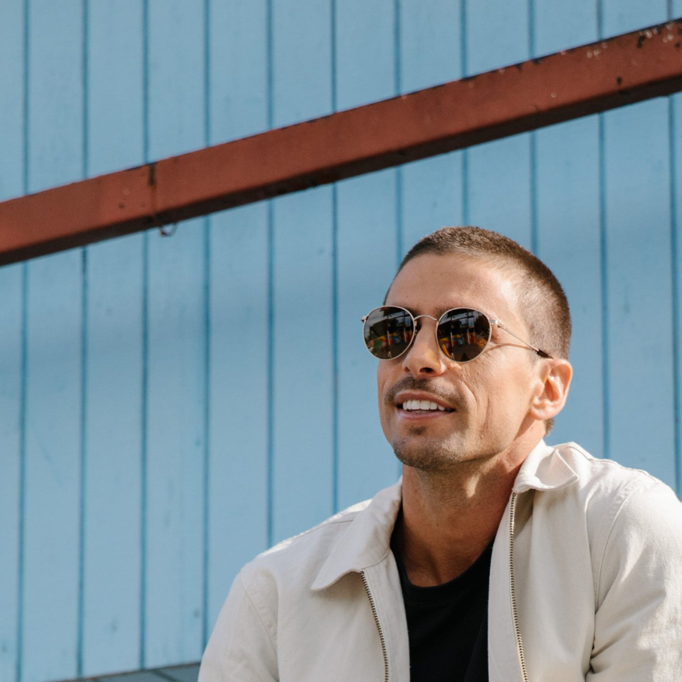 Man wearing round wire frame sunglasses in front of a blue wall