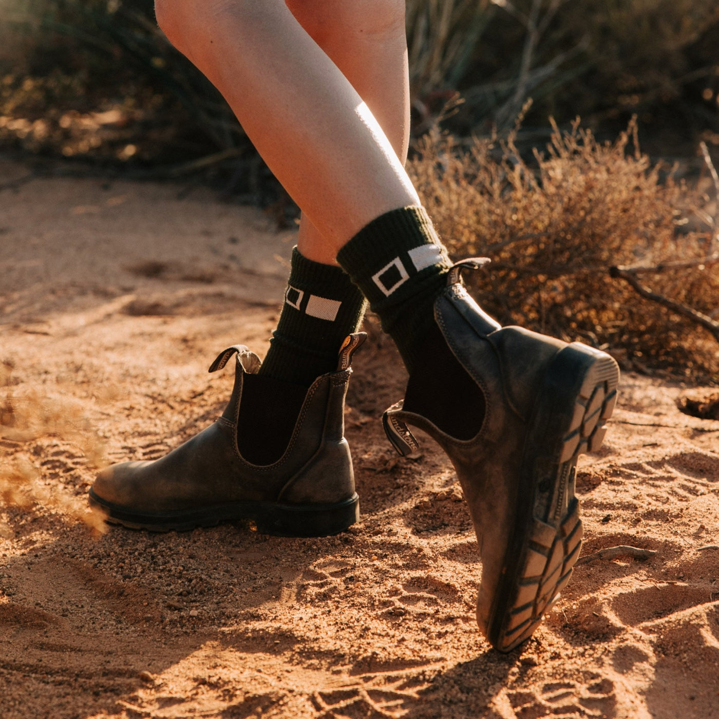 Someone wearing boots and socks walking on red dirt