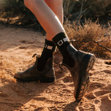 Someone wearing boots and socks walking on red dirt