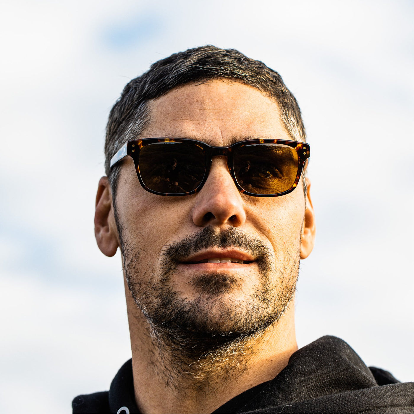Jay Davies wearing dark tort OTIS Eyewear sunglasses smiling