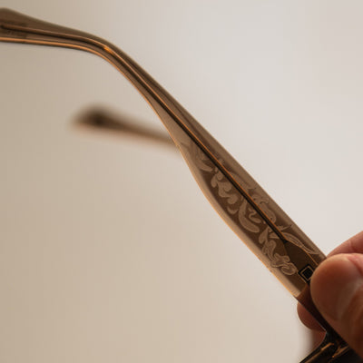 Brown sunglasses with artistic etching being held in someones hand