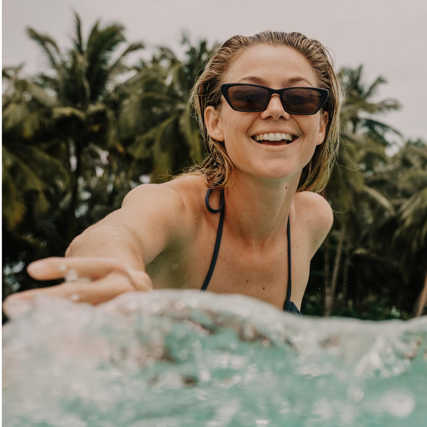 Imogen Caldwell playfully splashing in the ocean wearing OTIS Eyewear sunglasses